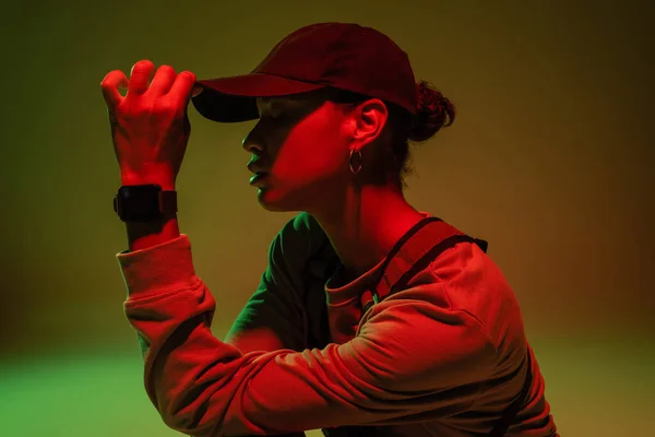 Side view of african american woman in sweatshirt adjusting baseball cap on green with red light — Photo de stock