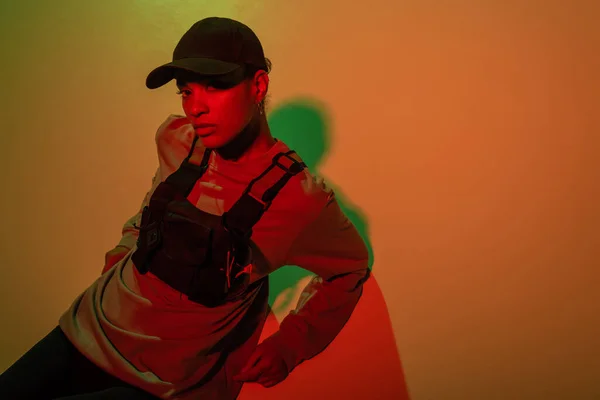 Top view of african american woman in baseball cap looking at camera on yellow with red light — Stockfoto