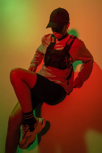 High angle view of african american woman in baseball cap lying on yellow with red light — Stockfoto