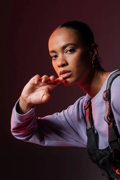 Young african american woman in sweatshirt looking at camera on dark purple — Stockfoto