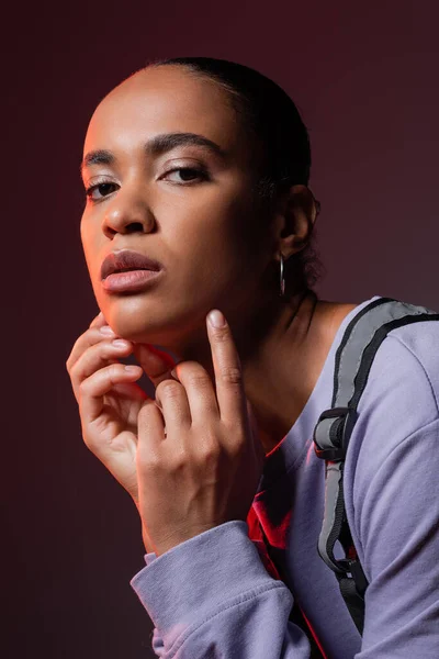 Молода афроамериканка в фіолетовому светрі і жилеті дивиться на камеру на темно-фіолетовому — стокове фото