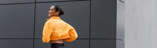 Cheerful african american sportswoman in yellow puffer jacket exercising outside, banner - foto de stock