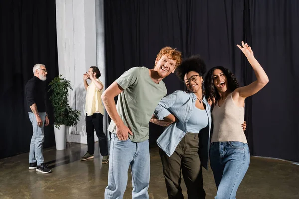 Excited multiracial actress waving hand near happy interracial team in theater — Foto stock