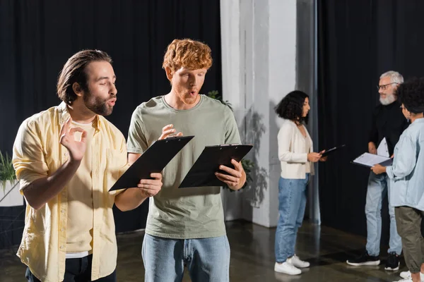 Brunette and red haired actors holding scenarios while grimacing and gesturing during rehearsal — стоковое фото