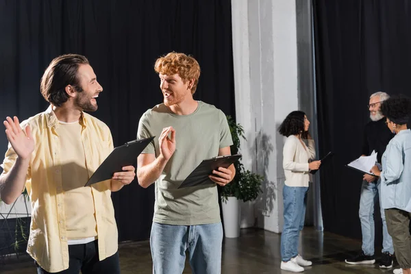 Happy young actors with clipboards gesturing during rehearsal in acting skills school — стоковое фото