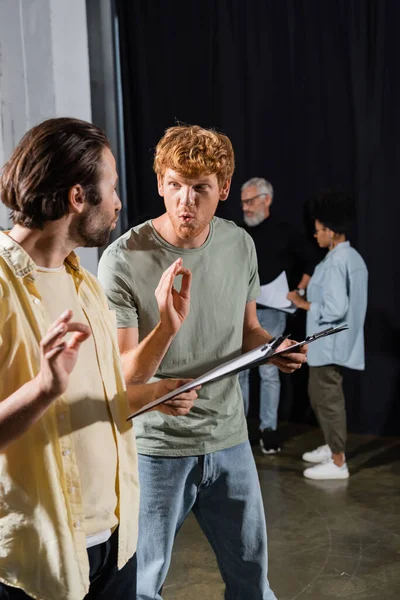Young actors with clipboards grimacing and showing okay signs during rehearsal in acting school — Stock Photo