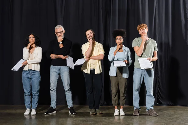 Full length of thoughtful multicultural actors with bearded grey haired art director holding scenarios while rehearsing on stage in theater — Photo de stock