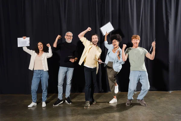 Excited interracial actors with mature art director rejoicing on stage and showing triumph gesture. Translation of tattoo: om, shanti, peace - foto de stock