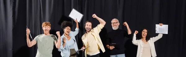 Excited multiracial actors holding screenplays and celebrating triumph near mature art director, banner. Translation of tattoo: om, shanti, peace — Stock Photo
