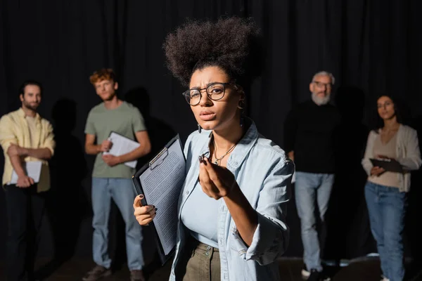 African american woman holding screenplay and gesturing during rehearsal near blurred actors and acting skills teacher — Stockfoto
