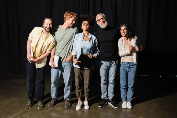 Молоді емоційні актори, що стоять на театральній сцені біля сіроволосих сценаристів — стокове фото