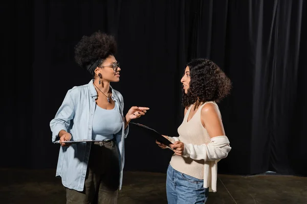 African american woman with clipboard pointing with finger while talking to multiracial actress in theater — Stockfoto