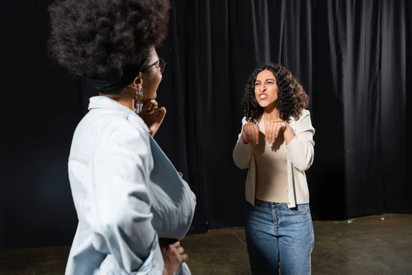 Multiracial actress showing hare near african american woman standing with hand on hip on blurred foreground — Stock Photo
