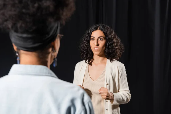 Multiracial actress grimacing while rehearsing near blurred african american actress in theater — Stock Photo