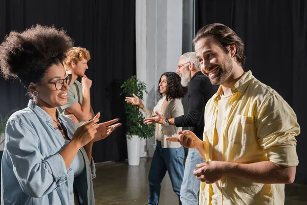 Side view of smiling multiethnic students and teacher of acting skills talking and gesturing in theater school — Foto stock