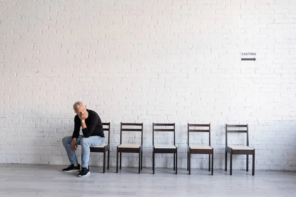 Сірошерстий актор середнього віку сидить на стільці в коридорі і чекає на кастинг — стокове фото