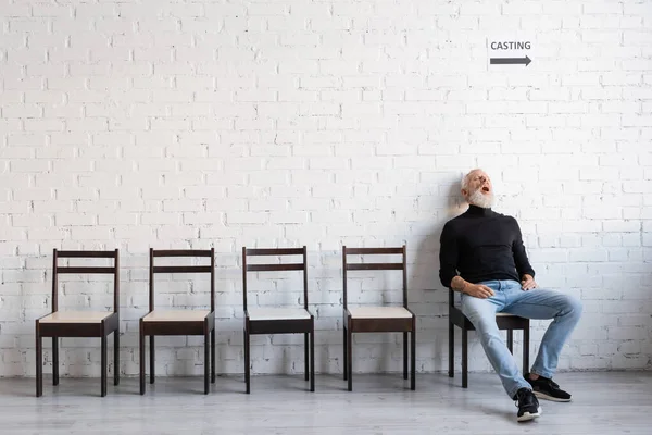 Full length of mature man sleeping on chair while waiting for casting on chair near white wall — стоковое фото