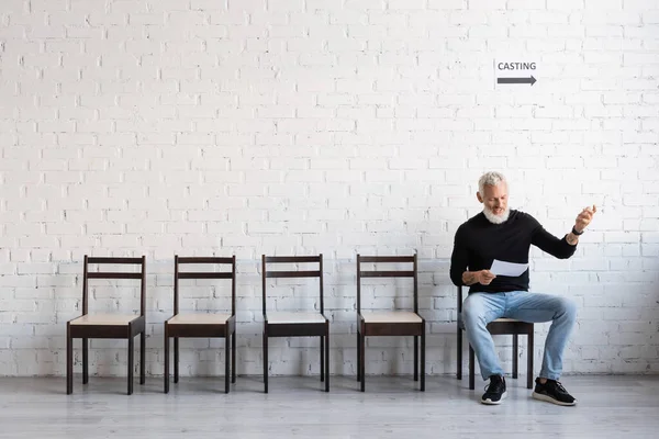 Bearded middle aged actor reading screenplay while waiting for casting in hall — Photo de stock