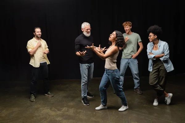 Multiracial woman gesturing while rehearsing near bearded art director and smiling interracial actors — Photo de stock