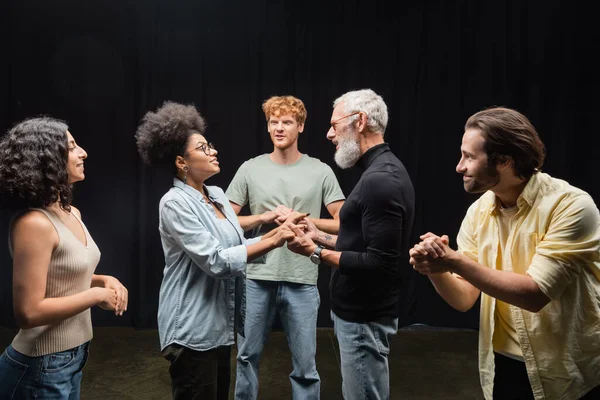 Bearded art director holding hands with african american actress near students in theater school. Translation of tattoo: kanji, danger - foto de stock