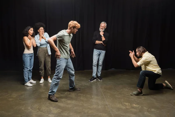 Young actors playing scene near grey haired art director and amazed interracial women. Translation of tattoo: om, shanti, peace — Stock Photo