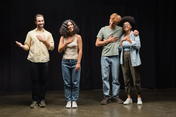 Повна довжина задоволених мультикультурних акторів тримає руки на грудях, стоячи на театральній сцені — стокове фото