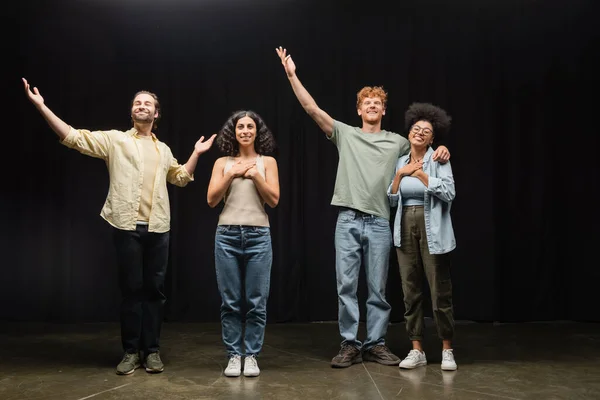 Повна довжина щасливих багатоетнічних акторів, що стоять з піднятими руками на сцені театру — стокове фото