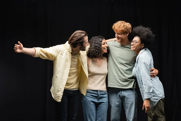 Young and pleased multicultural actors hugging and smiling at each other in theater school — Photo de stock