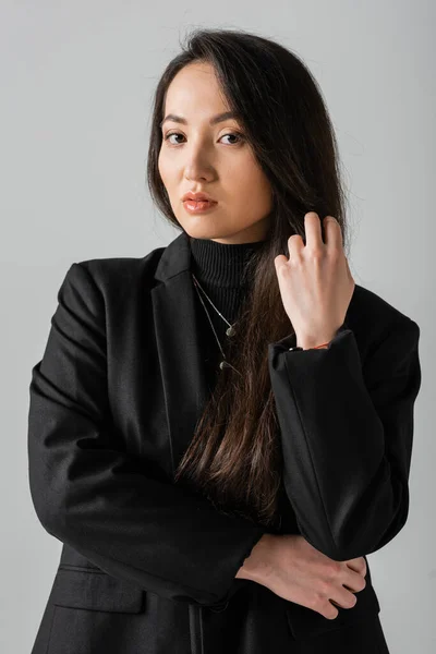 Portrait of young asian businesswoman in black suit standing and looking at camera isolated on grey — Stock Photo