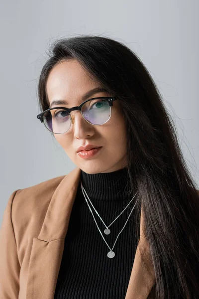 Portrait of brunette asian businesswoman in beige blazer and glasses isolated on grey — Stock Photo