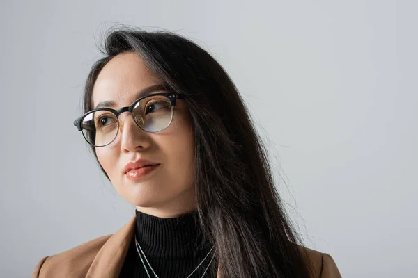 Portrait of brunette asian businesswoman in beige blazer and glasses looking away isolated on grey — Stock Photo