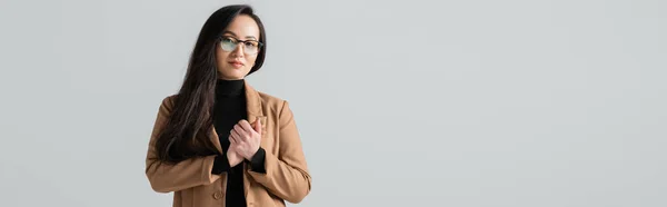 Young asian businesswoman in glasses and beige blazer standing with clenched hands isolated on grey, banner — Stock Photo