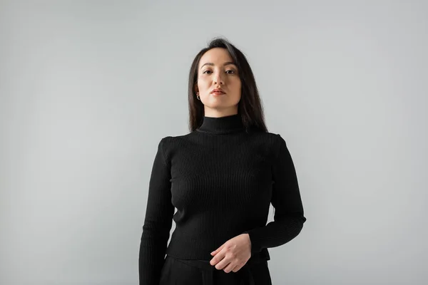 Asian businesswoman in black turtleneck looking at camera isolated on grey - foto de stock