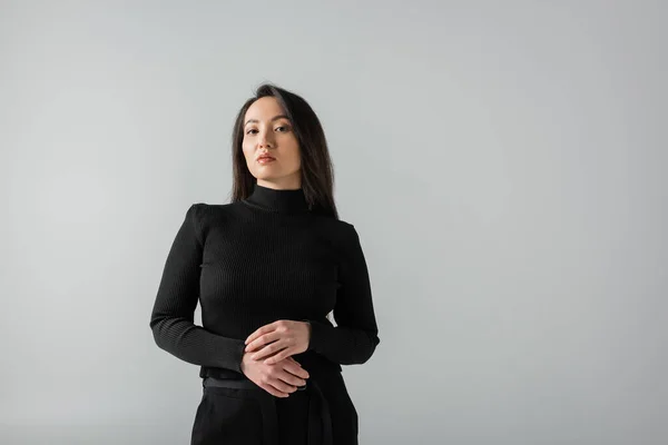 Brunette asian businesswoman in black turtleneck looking at camera isolated on grey - foto de stock