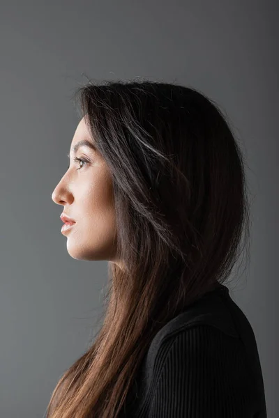 Side view of brunette and asian woman in black turtleneck looking away isolated on dark grey — Stockfoto