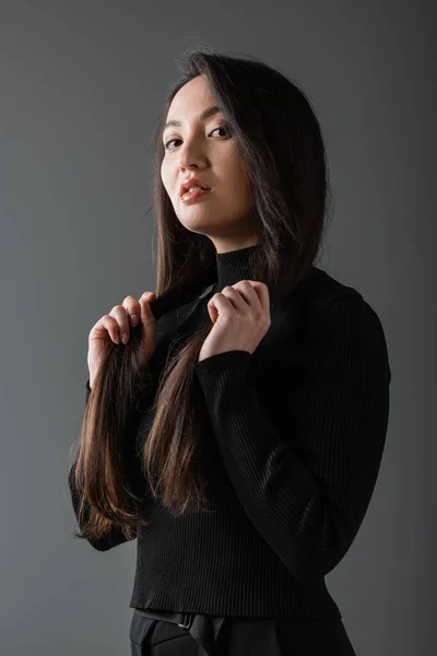 Portrait of brunette and asian woman in black turtleneck looking at camera isolated on dark grey — Stock Photo