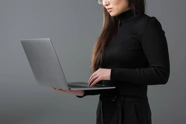 Обрізаний вид жінки в чорному черепашку з використанням ноутбука ізольовано на темно-сірому — стокове фото