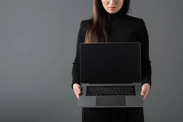 Cropped view of young woman in black turtleneck showing laptop with blank screen isolated on dark grey — Foto stock