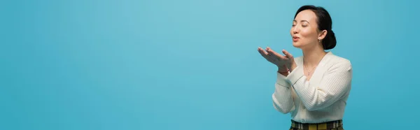 Young asian woman with closed eyes sending air kiss isolated on blue, banner — стоковое фото