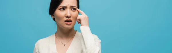 Pensive young asian woman looking away isolated on blue, banner — Stock Photo