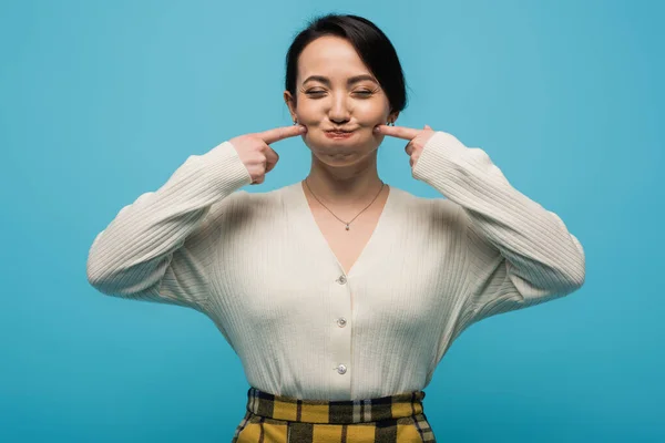 Young asian woman grimacing and touching cheeks isolated on blue — Stock Photo