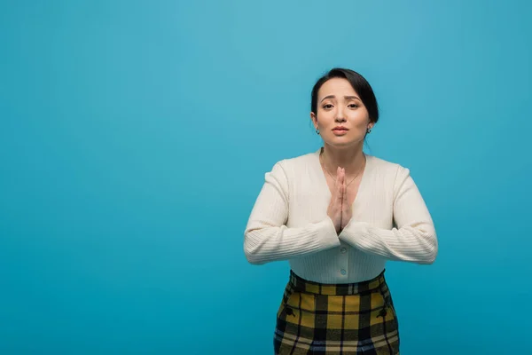 Asian woman in cardigan showing praying hands gesture isolated on blue — Photo de stock