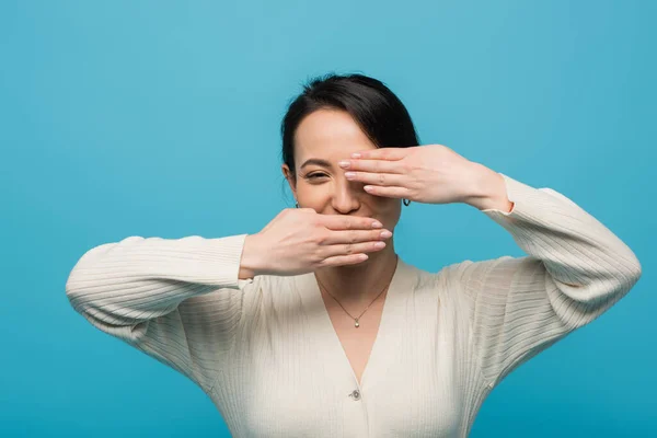 Brunette asian woman covering face isolated on blue — стоковое фото