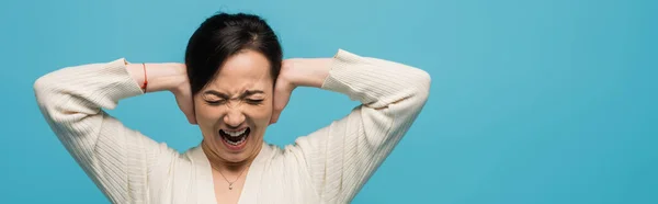 Aggressive asian woman screaming and covering ears isolated on blue, banner — Photo de stock