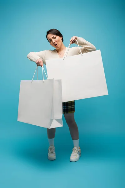 Confident asian woman holding shopping bags on blue background - foto de stock