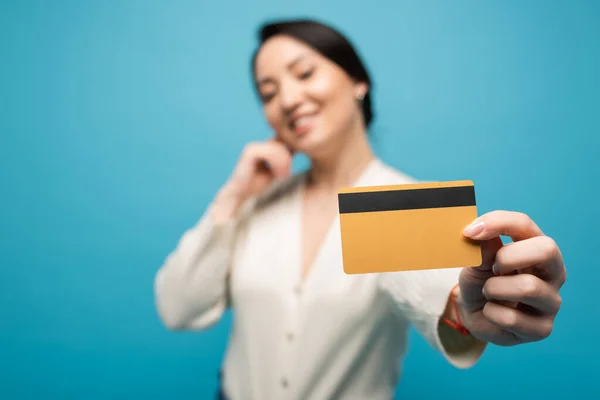 Asian and brunette woman showing credit card isolated on blue — стоковое фото
