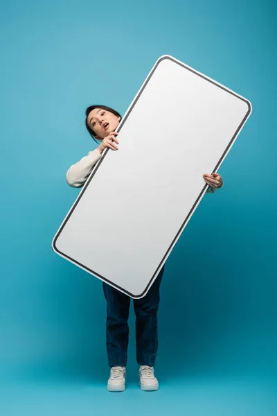 Confused asian woman holding big smartphone model on blue background — Stockfoto