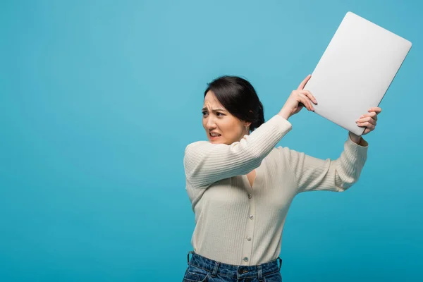 Aggressive asian freelancer throwing laptop isolated on blue — стоковое фото