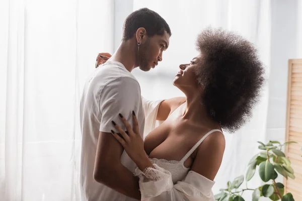 Vista lateral do casal de amantes afro-americanos abraçando e olhando uns para os outros em casa — Fotografia de Stock