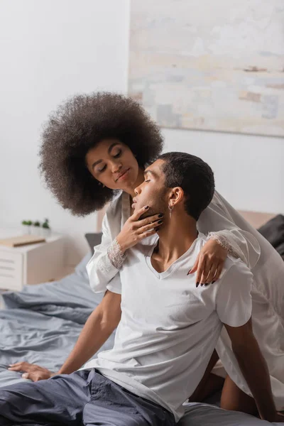 Curly african american woman seducing young man in white t-shirt on bed at home — Stock Photo